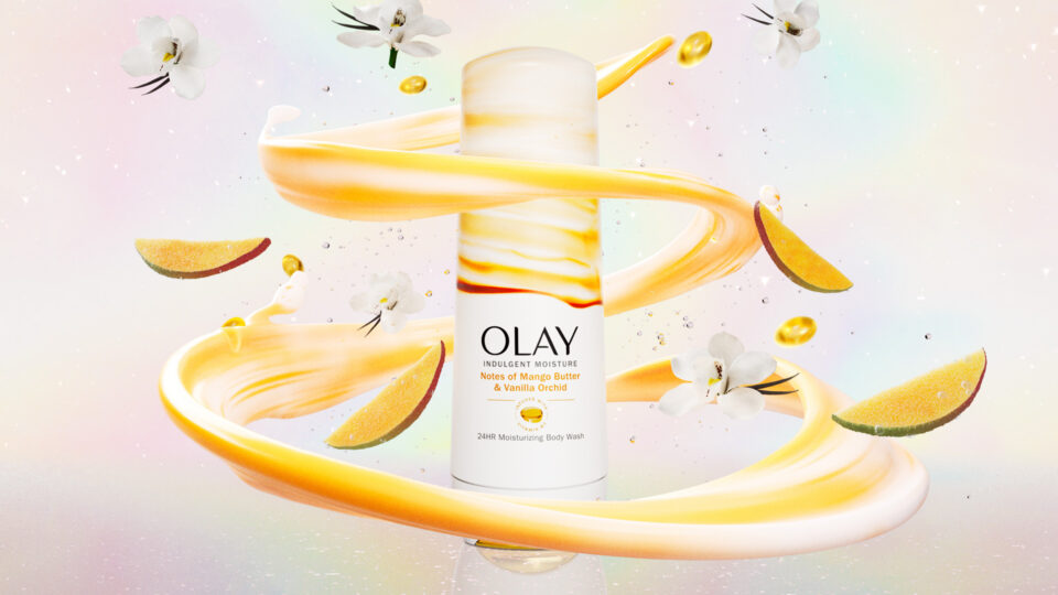 Olay body wash bottle surrounded by mango slices and orchid flowers in swirling golden liquid.