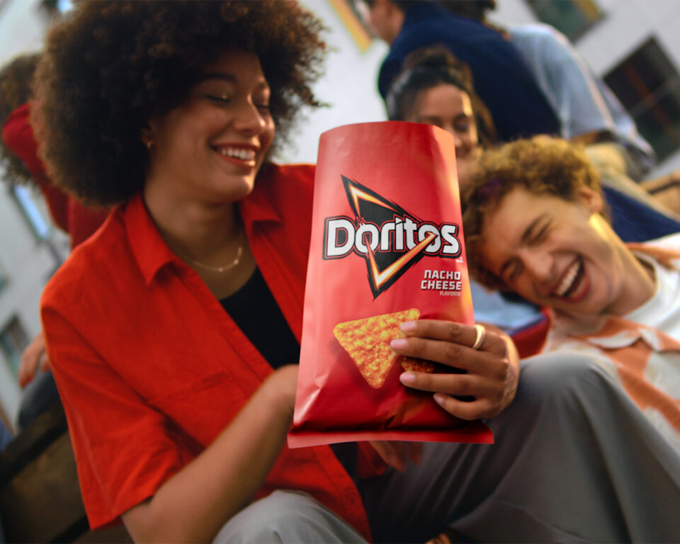 Friends laughing while holding a bag of Doritos Nacho Cheese chips.