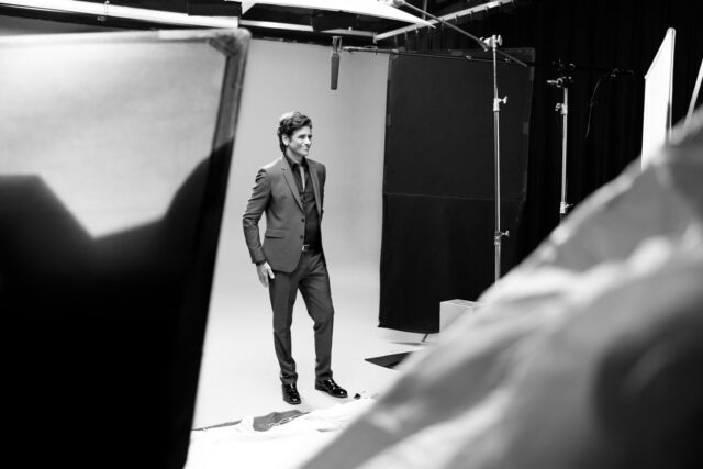 John Stamos in suit posing in studio with lighting equipment visible