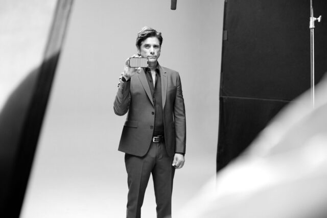 John Stamos in suit holds phone, studio shot, black and white